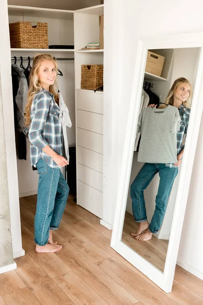 Young smiling woman fitting grey tshirt in front of mirror at home — Stock Photo