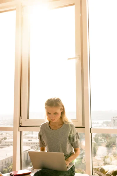 Молодая женщина использует ноутбук, сидя у окна дома — стоковое фото