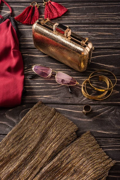 Vista de perto da bolsa feminina vermelha e dourada na moda, óculos de sol e jóias na mesa de madeira — Fotografia de Stock