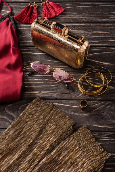 Vue rapprochée du sac à main féminin rouge et doré à la mode, des lunettes de soleil et des bijoux sur la table en bois — Photo de stock