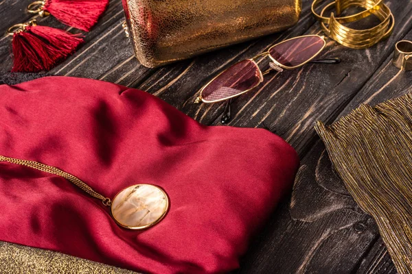 Nahaufnahme der modischen rot-goldenen Damenhandtasche, Sonnenbrille und Kleidung auf Holztischplatte — Stockfoto