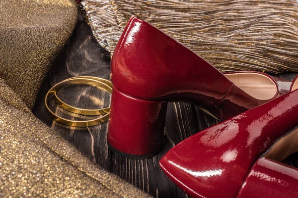 Nahaufnahme von modischen roten und goldenen Damenschuhen und Armbändern auf hölzerner Tischplatte — Stockfoto