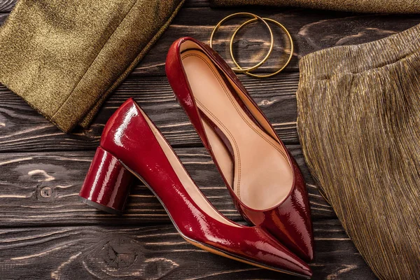 Vista de perto da moda sapatos femininos vermelhos e dourados e pulseiras na mesa de madeira — Fotografia de Stock