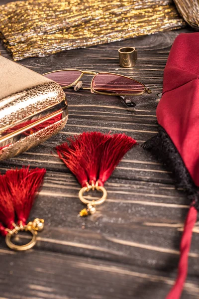 Close up view of fashionable feminine earrings, sunglasses and purse arranged on wooden tabletop — Stock Photo
