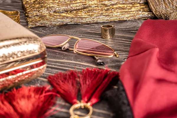 Vue rapprochée des boucles d'oreilles féminines à la mode, des lunettes de soleil et du sac à main disposés sur une table en bois — Photo de stock