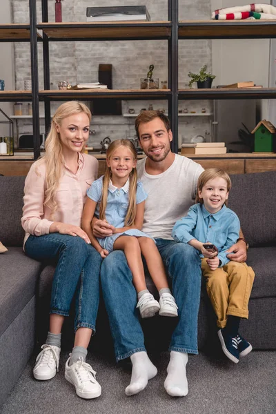 Glückliche junge Familie sitzt zusammen auf der Couch und blickt in die Kamera — Stockfoto