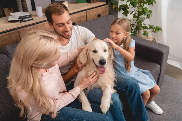 Aus der Vogelperspektive: Eltern mit Tochter spielen mit Hund, während sie zu Hause auf der Couch sitzen — Stockfoto