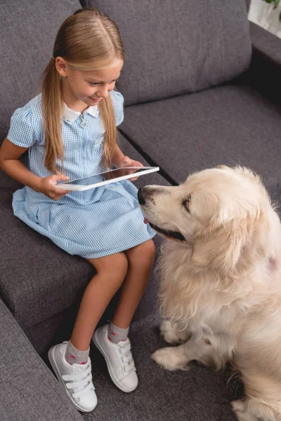 Hochwinkelaufnahme eines glücklichen kleinen Kindes mit Labrador-Hund mit Tablet im Sitzen auf der Couch — Stockfoto