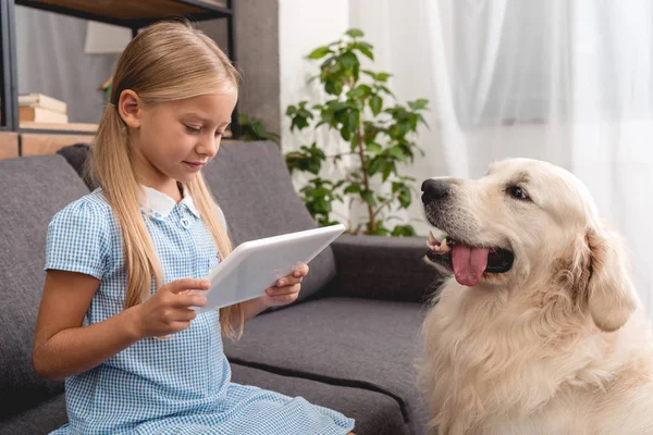 Entzückendes kleines Kind mit Labrador-Hund mit Tablet auf der Couch — Stockfoto