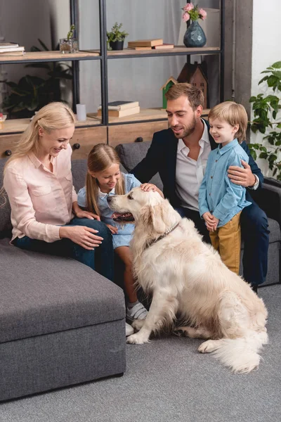 Happy young family playing with dog while sitting on couch at home — Stock Photo
