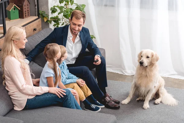 Высокий угол зрения счастливой молодой семьи, сидящей дома на диване с собакой — стоковое фото