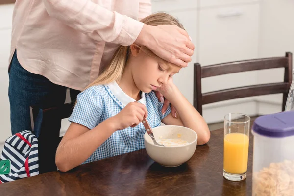 Cropped shot of mother checking little daughters temperature with hand while she having breakfast — Stock Photo