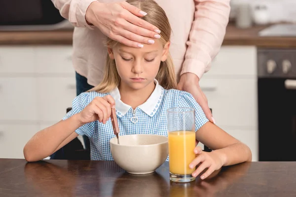 Cropped shot of mother checking daughters temperature with hand while she having breakfast — Stock Photo