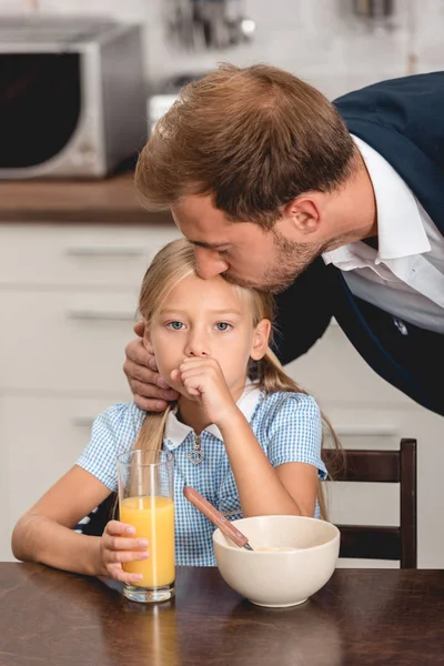 Young father checking temperature of sick daughter with lips during breakfast — Stock Photo