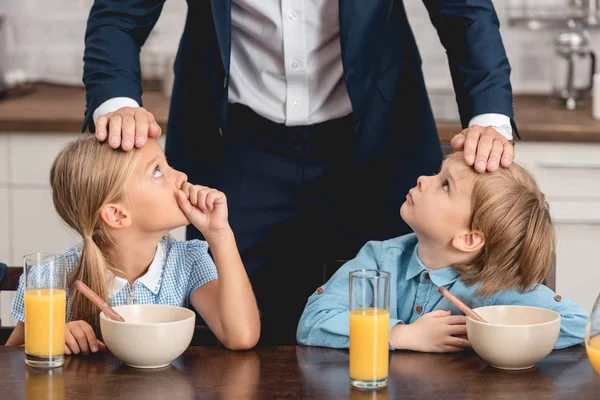 Recortado tiro fo padre comprobar la temperatura de sus hijos enfermos tocando sus frentes durante el desayuno - foto de stock