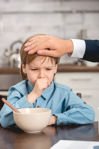 Schnappschuss vom Vater, der beim Frühstück die Temperatur seines kranken Sohnes mit der Hand überprüft — Stockfoto