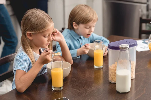 Lindos niños pequeños teniendo cereal para el desayuno juntos en la cocina - foto de stock