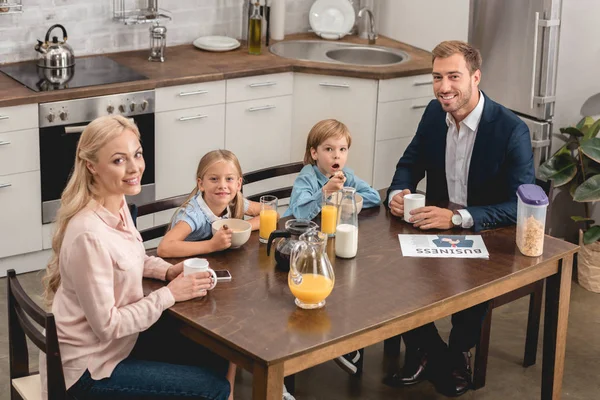 Heureuse jeune famille prenant le petit déjeuner ensemble à la cuisine et regardant la caméra — Photo de stock