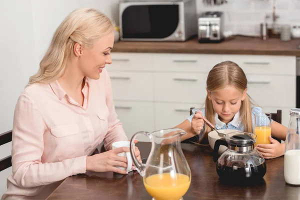 Улыбающиеся мать и дочь завтракают вместе на кухне — стоковое фото