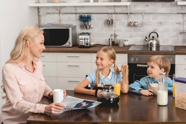 Happy mother having cup of coffee while sitting at kitchen with kids during breakfast — Stock Photo