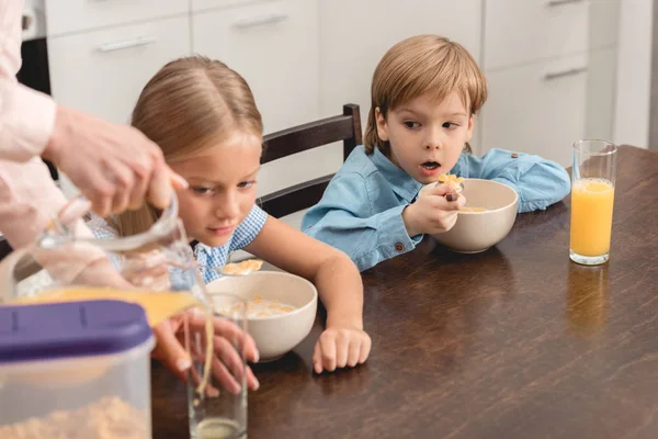 Cropped shot of mother pouring orange juice for adorable little kids during breakfast — Stock Photo