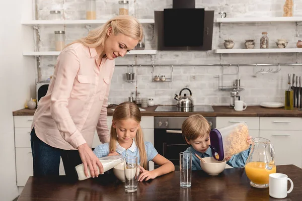 Mother pouring milk into cereal for adorable little kids during breakfast — Stock Photo