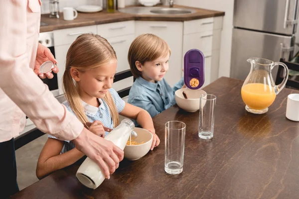 Cropped shot of mother pouring milk into cereal for adorable little kids during breakfast — Stock Photo