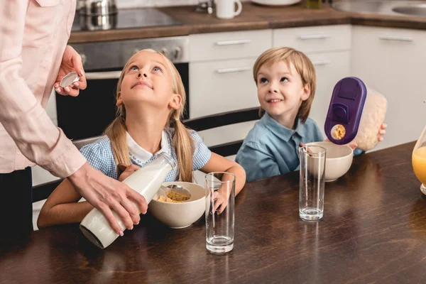 Cropped shot of mother pouring milk into cereal for happy little kids during breakfast — Stock Photo