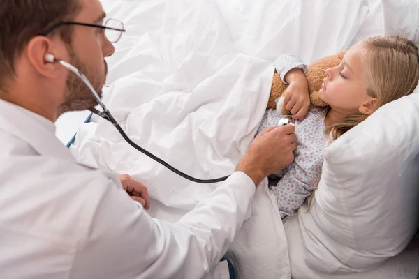 High angle view of pediatrician litening childs breath with stethoscope while she lying in bed — Stock Photo