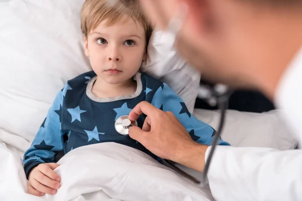 Primer plano tiro de pediatra litening niños respiración con estetoscopio mientras él acostado en la cama - foto de stock