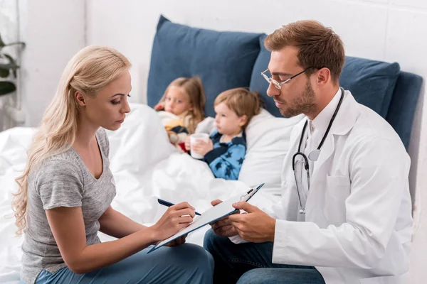 Pediatrician and mother and kids lying in bed — Stock Photo