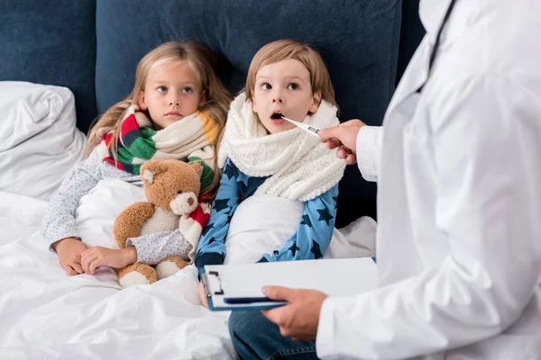 Schnappschuss von Kinderarzt mit Klemmbrett zur Untersuchung der Temperatur von Kindern, die im Bett liegen — Stockfoto