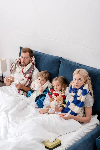 High angle view of sick young family sitting in bed together and looking at camera — Stock Photo