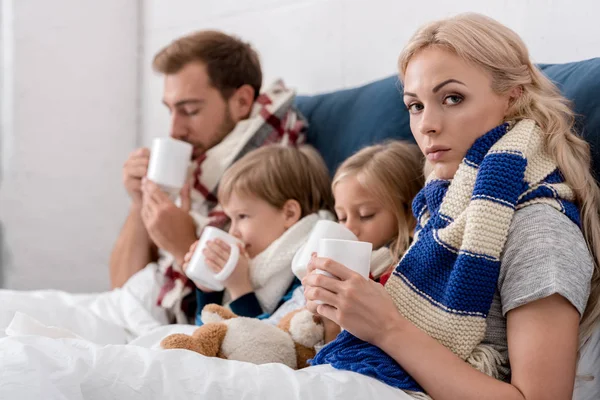 Diseased young family drinking warming beverages in bed — Stock Photo