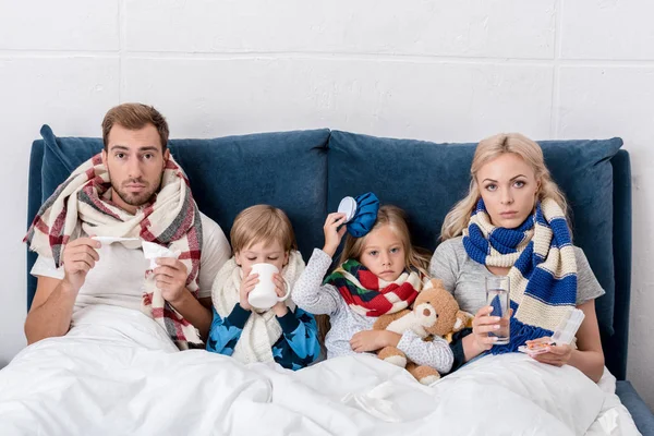 Malade jeune famille assis dans le lit ensemble et regardant caméra — Photo de stock