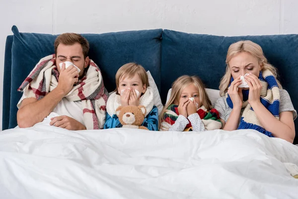 Sick young family blowing noses with napkins together while lying in bed — Stock Photo