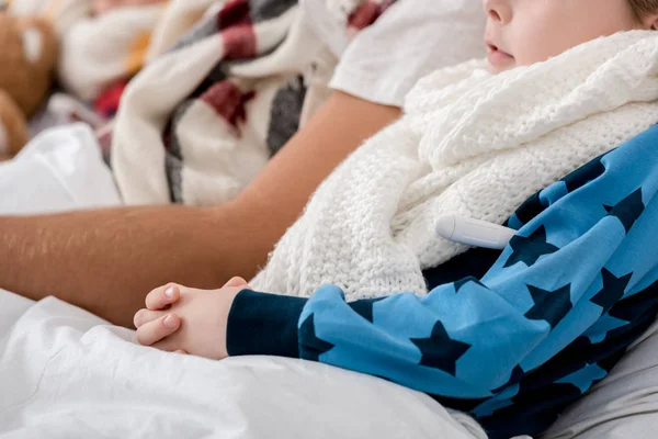 Cropped shot of sick father and son in scarves lying in bed together — Stock Photo