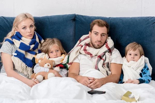 Kranke junge Familie in Schals blickt im Bett in die Kamera — Stockfoto