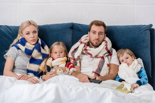 Sick young family in scarves looking at camera while lying in bed — Stock Photo