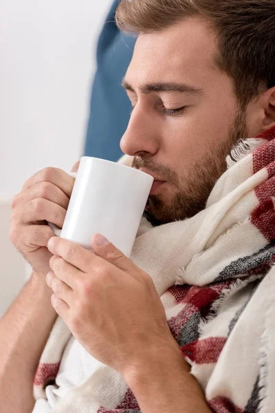 Primer plano retrato de hombre joven enfermo en bufanda con taza de té - foto de stock
