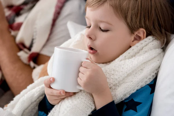 Портрет малыша в шарфе с чашкой горячего напитка в постели — стоковое фото