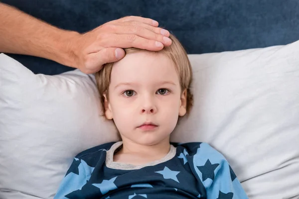 Tiro cortado de pai verificando a temperatura dos filhos com a mão enquanto ele deitado na cama — Fotografia de Stock