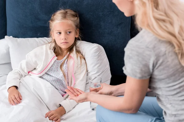 Plan recadré de mère donnant des pilules et de l'eau à sa fille malade au lit — Photo de stock