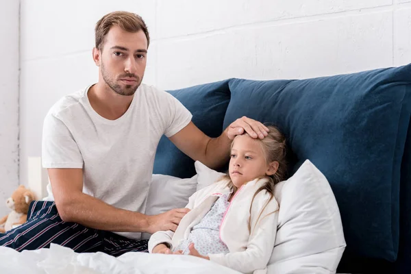 Vater überprüft Temperatur der Töchter mit der Hand, während sie im Bett liegt — Stockfoto