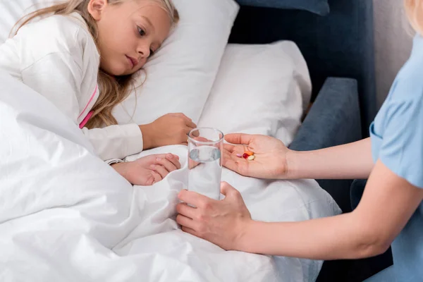 Inyección recortada de la madre dando pastillas y agua a su hija enferma - foto de stock