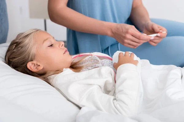 Schnappschuss einer Mutter, die die Temperatur ihrer Töchter mit einem elektrischen Thermometer überprüft — Stockfoto