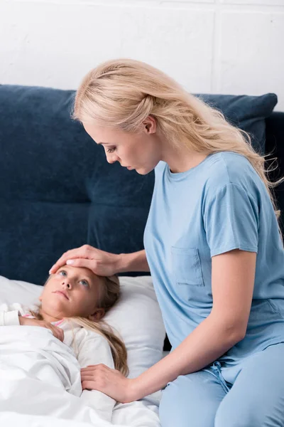 Jovem mãe verificando suas filhas doentes temperatura com a mão — Fotografia de Stock