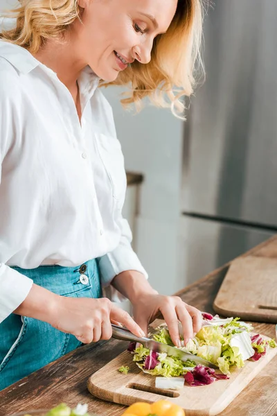 Tiro de close-up de mulher adulta feliz cortando alface para salada na cozinha — Fotografia de Stock