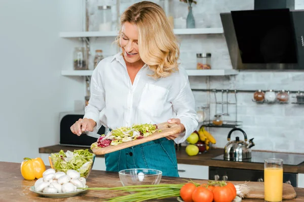 Hermosa mujer adulta haciendo ensalada saludable en la cocina - foto de stock