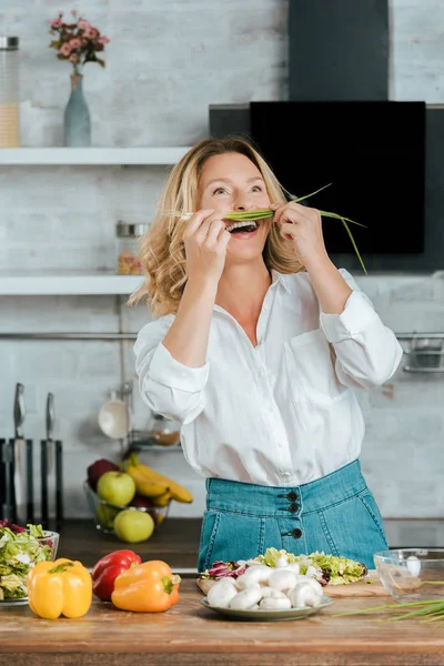 Смеющаяся взрослая женщина прикрепляет лук-порей как усы на кухне — стоковое фото